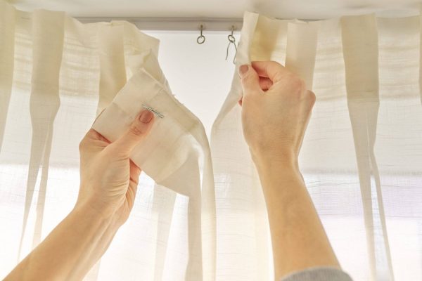 Close up of woman hands hanging curtain with metal hooks on ceiling ledge.