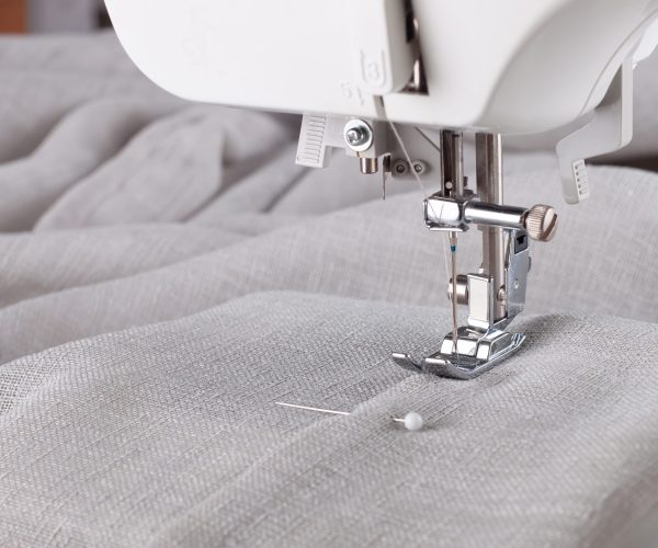 Modern sewing machine presser foot with linen fabric and thread, closeup, copy space. Sewing process clothes, curtains, upholstery. Business, hobby, handmade, zero waste, recycling, repair concept