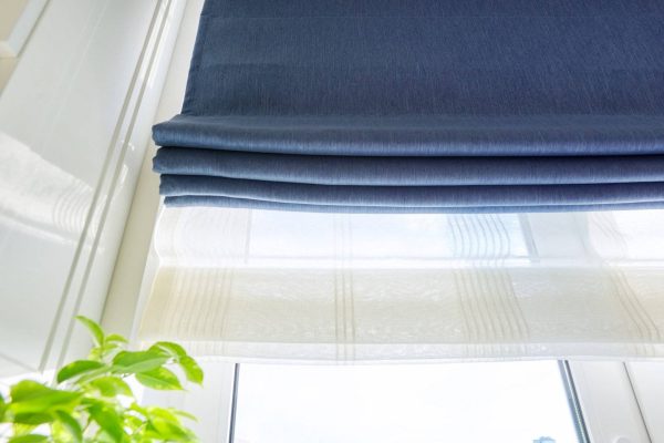 Roman blind in the interior detail close-up. Curtain blue blackout fabric, sheers white linen, fashionable modern window decoration design at home